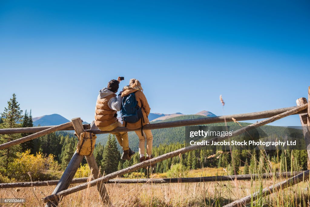 Hispanic couple on wooden fence photographing mountains