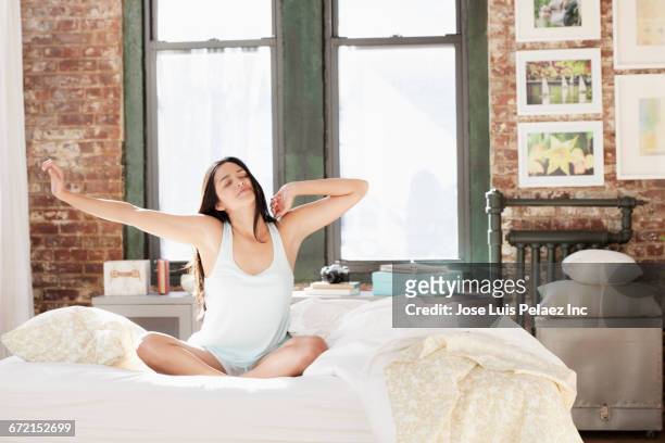 hispanic woman waking in morning and stretching arms - morning bed stretch stock-fotos und bilder