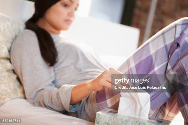 hispanic woman wearing pajamas pulling tissue from box - tissue box stockfoto's en -beelden