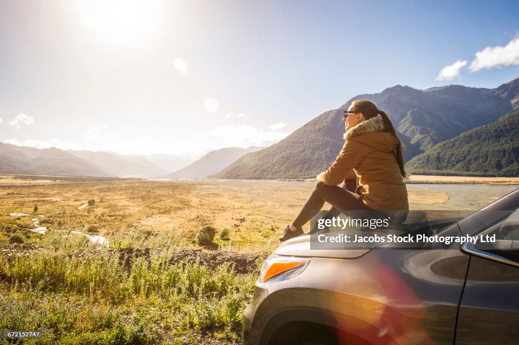 Hispanic woman sitting on hood of car admiring scenic view