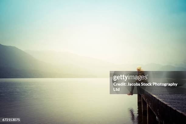 distant hispanic woman wearing coat sitting on dock at mountain lake - pier 1 stock pictures, royalty-free photos & images