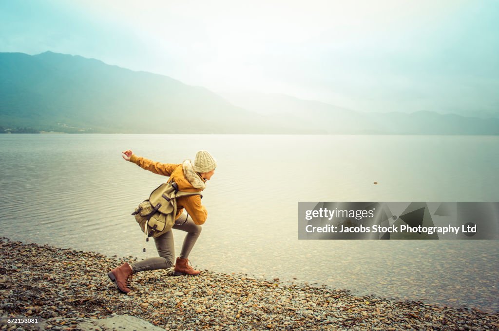 Hispanic woman wearing coat skipping rock at mountain lake