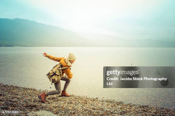 hispanic woman wearing coat skipping rock at mountain lake - throwing rocks stock pictures, royalty-free photos & images