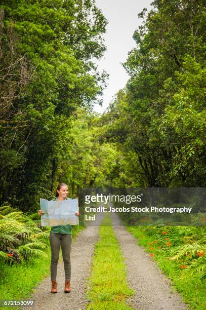 hispanic woman reading map on path in lush green forest - グレイマウス ストックフォトと画像