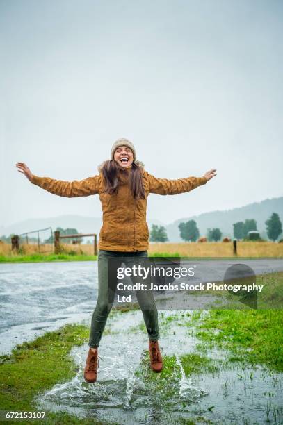 laughing hispanic woman splashing in puddle - puddle fotografías e imágenes de stock