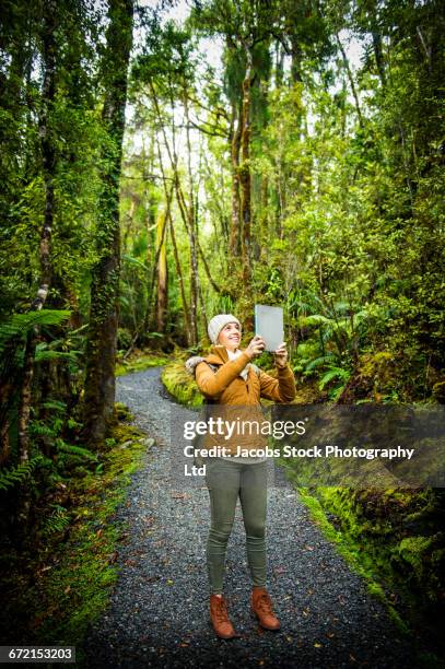 hispanic woman on path in lush green forest photographing with digital tablet - eisstockschießen stock-fotos und bilder