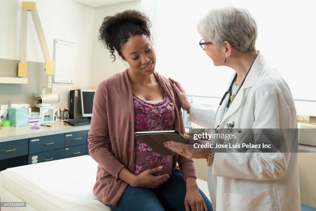 Gynecologist with digital tablet comforting pregnant patient