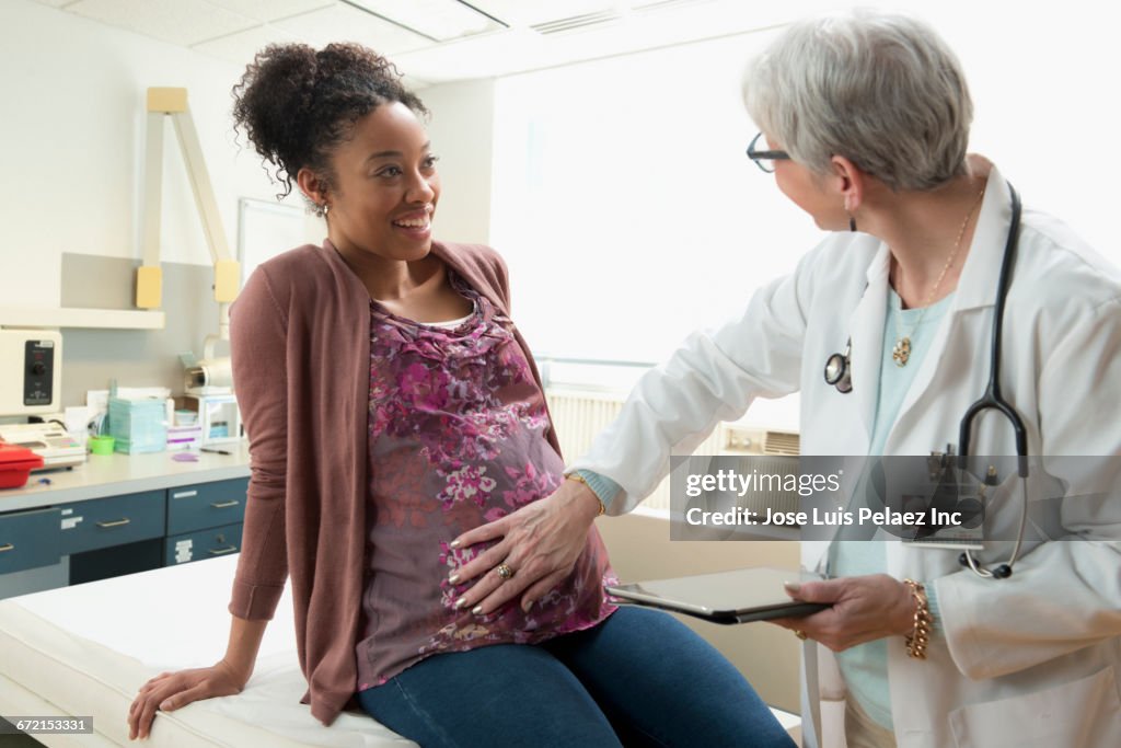 Gynecologist with digital tablet feeling belly of pregnant patient