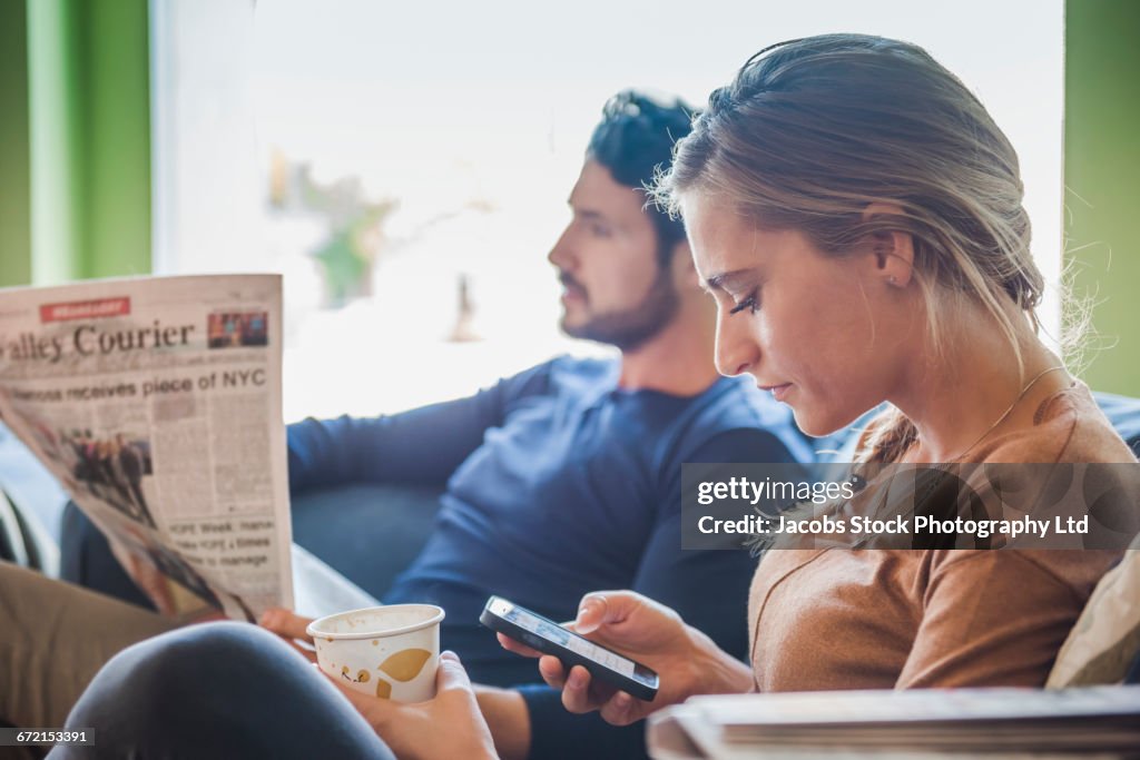Hispanic couple with newspaper and cell phone in coffee shop