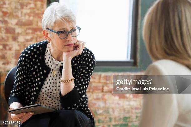 caucasian businesswomen talking in office with digital tablet - mental health professional stock pictures, royalty-free photos & images