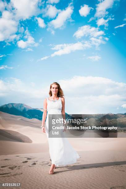 hispanic woman in white gown walking on sand dune - white dress stock-fotos und bilder