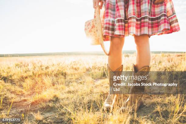 legs of hispanic woman wearing cowboy boots holding hat in desert - cowboystövlar bildbanksfoton och bilder