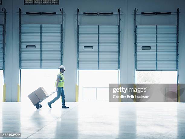 indian worker pulling hand truck near open loading dock doors - muelle de carga fotografías e imágenes de stock