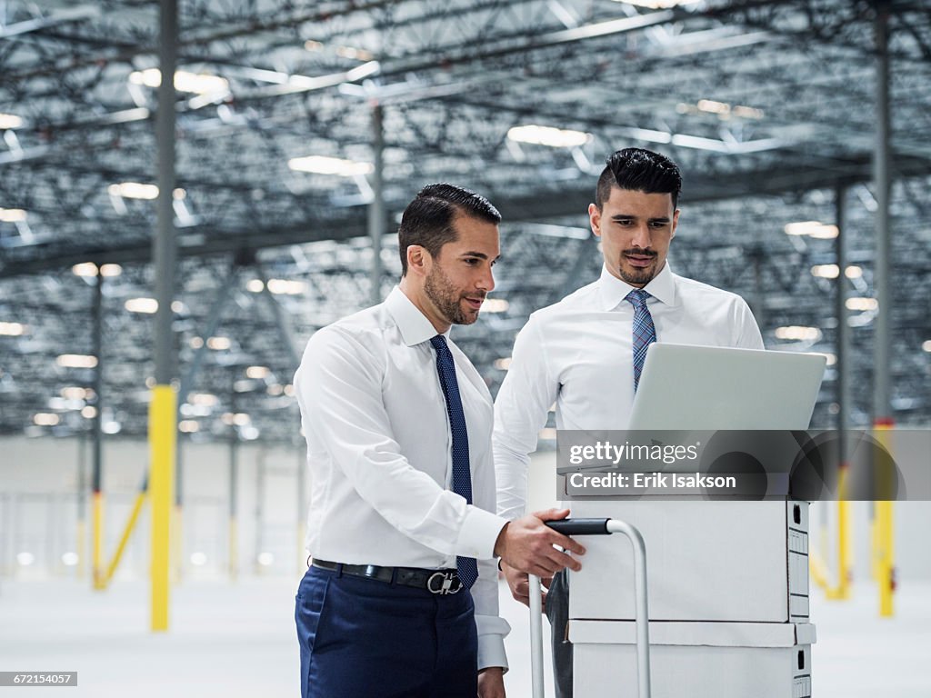 Businessmen using laptop on cardboard boxes in warehouse