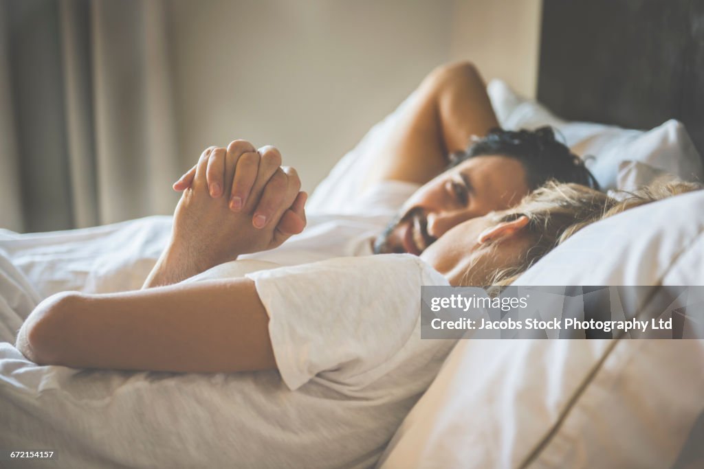 Hispanic couple holding hands in bed