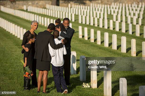 multi-generation black family hugging in military cemetery - african american funeral stock pictures, royalty-free photos & images