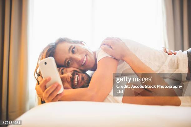 cuddling hispanic couple taking selfie on bed - guancia a guancia foto e immagini stock