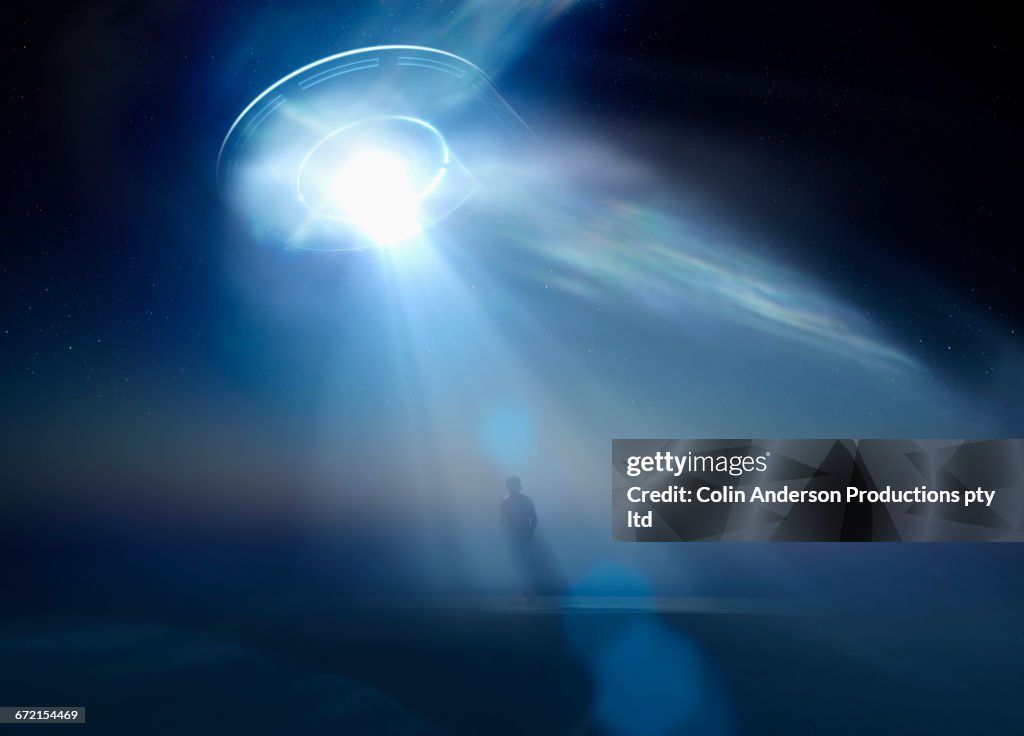 Caucasian man standing in beam of light from UFO