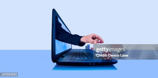 hand holding gambling chips emerging from laptop screen - jogos de azar imagens e fotografias de stock