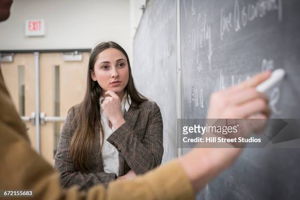 caucasian man and woman writing on blackboard in classroom - two female teachers blackboard stockfoto's en -beelden