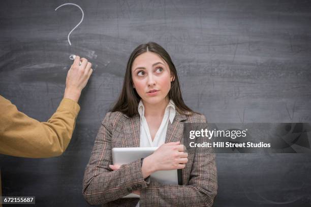 caucasian woman thinking next to question mark on blackboard in classroom - fragen stock-fotos und bilder