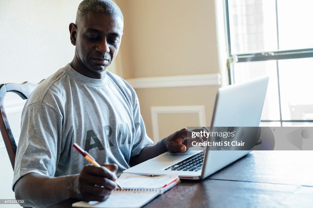 Black man using laptop and notebook at table