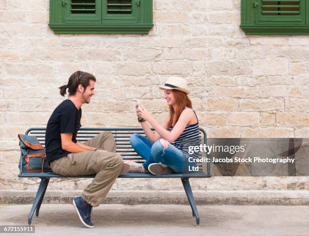 smiling woman sitting on bench photographing man with cell phone - bench stock pictures, royalty-free photos & images