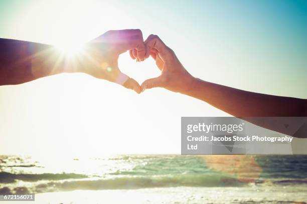 caucasian couple making heart symbol with hands at beach - myrtle beach foto e immagini stock