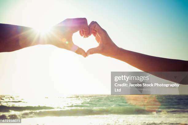 caucasian couple making heart symbol with hands at beach - two hearts stock pictures, royalty-free photos & images