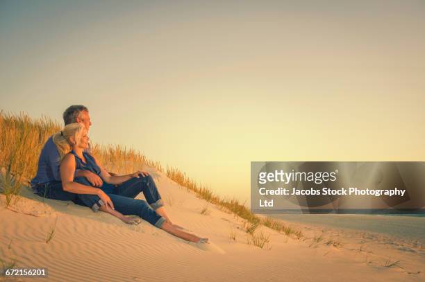 caucasian couple sitting on sand dune at beach - myrtle beach imagens e fotografias de stock