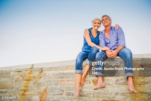 caucasian couple hugging on wall at beach - 45 couple stockfoto's en -beelden