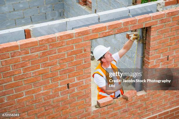 caucasian construction worker laying bricks and using measuring tape - pedreiro imagens e fotografias de stock