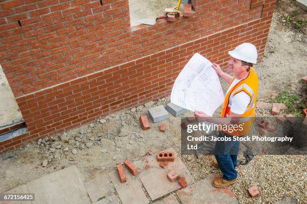 caucasian construction worker reading blueprint at brick wall - spalding place bildbanksfoton och bilder