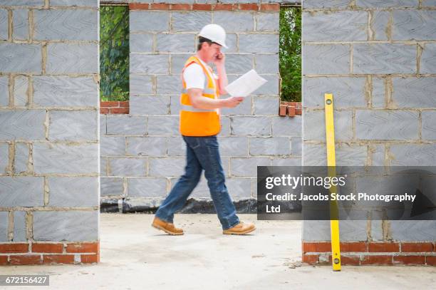 caucasian construction worker reading blueprint and talking on cell phone - doorway stock pictures, royalty-free photos & images