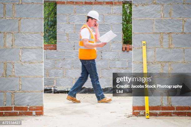 caucasian construction worker reading blueprint and talking on cell phone - spalding place bildbanksfoton och bilder