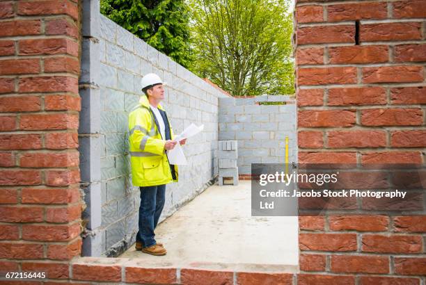 caucasian construction foreman checking blueprint at brick wall - spalding place bildbanksfoton och bilder