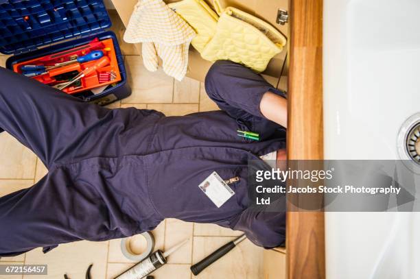 caucasian plumber working under sink - plumber stockfoto's en -beelden