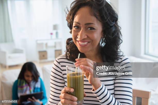 mother drinking green smoothie while daughter uses digital tablet - mature woman smoothie stock-fotos und bilder