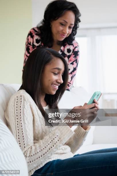 mother watching daughter use cell phone on sofa - private viewing stock-fotos und bilder