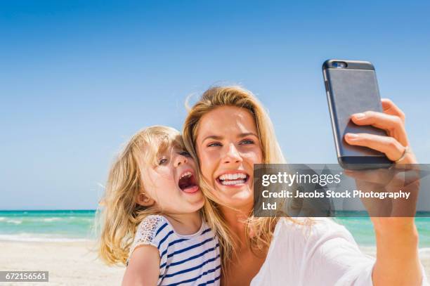 caucasian mother and daughter posing for cell phone selfie at beach - blonde woman selfie foto e immagini stock