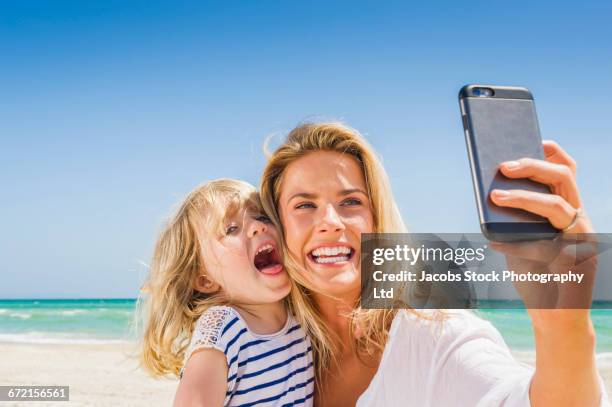 caucasian mother and daughter posing for cell phone selfie at beach - blonde woman selfie stockfoto's en -beelden