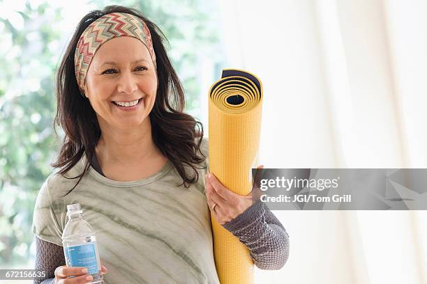 smiling hispanic woman holding exercise mat and water bottle - headband stock pictures, royalty-free photos & images