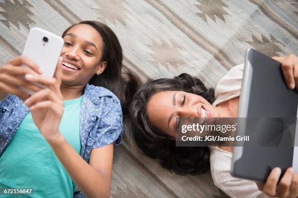 mother and daughter laying on carpet using cell phone and digital tablet - family teenager home life stock pictures, royalty-free photos & images