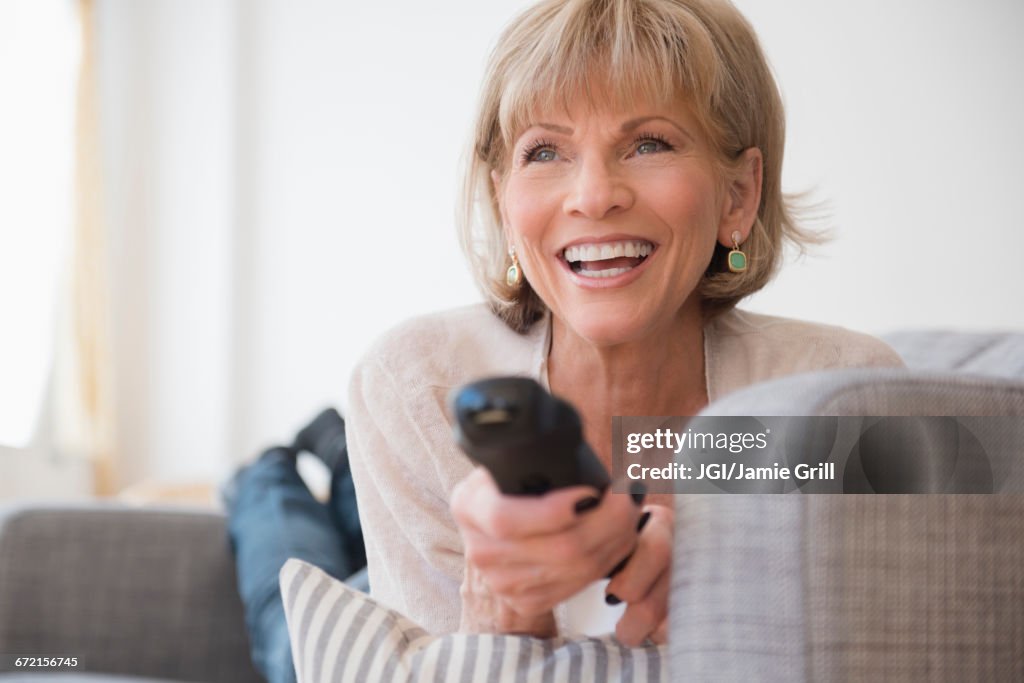 Older Caucasian woman laying on sofa watching television