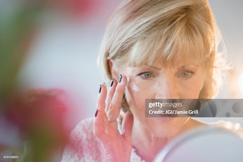 Older Caucasian woman applying moisturizer to face