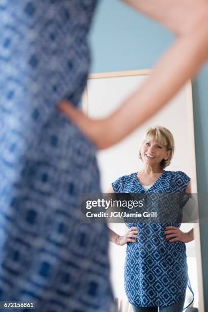 older caucasian woman admiring dress in mirror - woman mirror dress stock-fotos und bilder