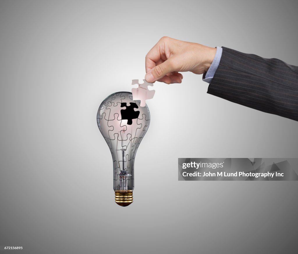 Hand of Caucasian businessman holding missing light bulb puzzle piece