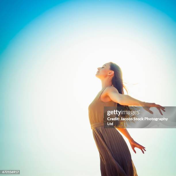 profile of caucasian woman against blue sky - 腕を広げる ストックフォトと画像