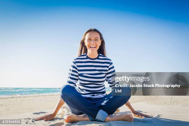 laughing caucasian woman sitting on sand at beach - con las piernas cruzadas fotografías e imágenes de stock