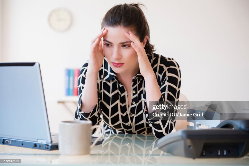 Caucasian businesswoman with headache using laptop